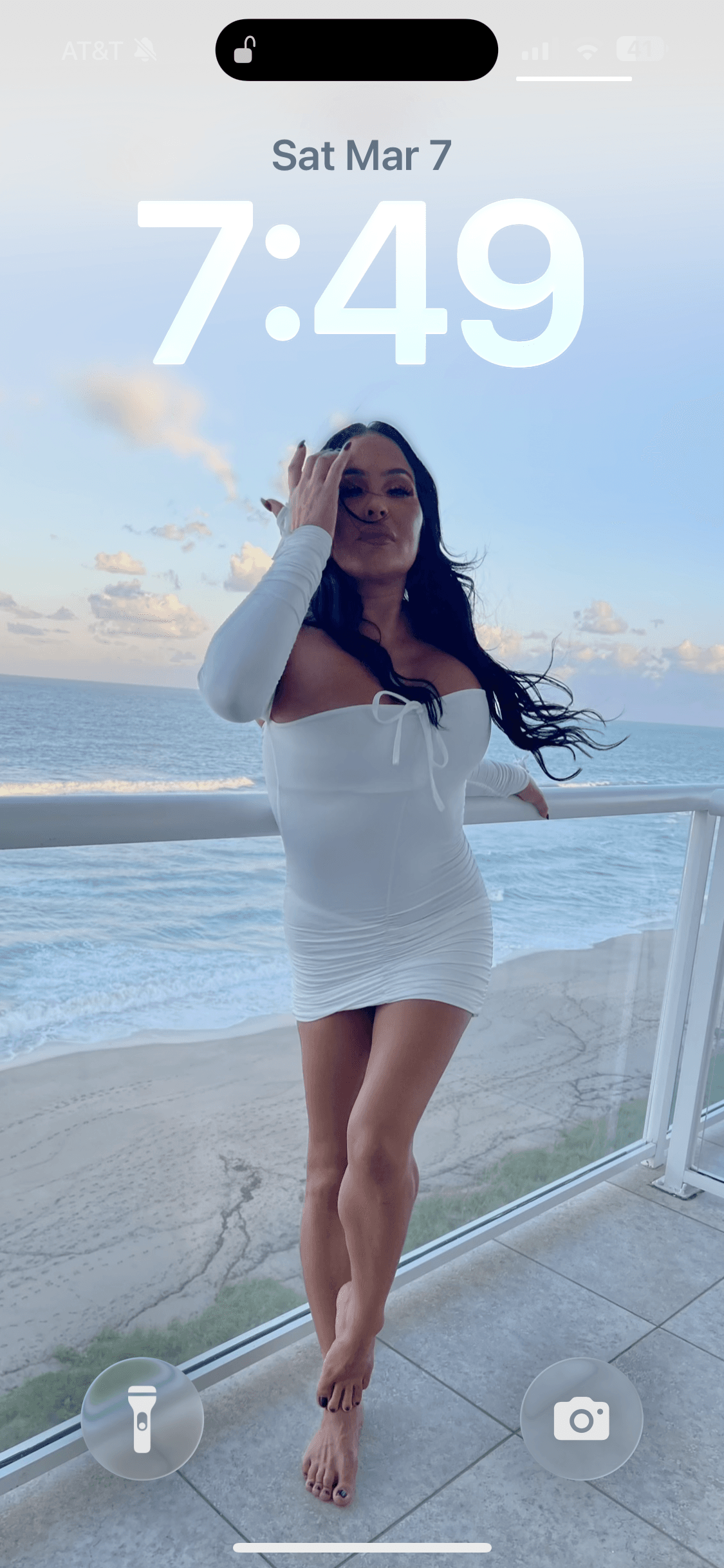 Woman in a short white dress posing on a balcony overlooking the beach and ocean.